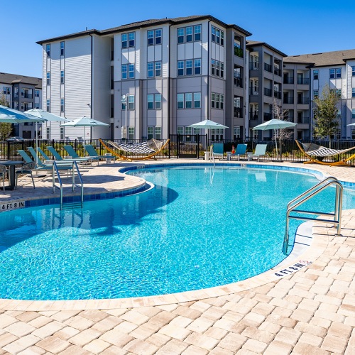 Luxury apartments in Kissimmee featuring a curved pool, sun umbrellas, and poolside hammocks.