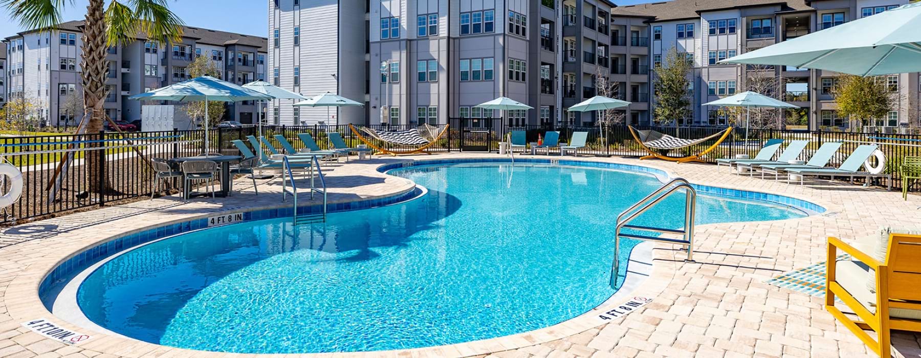 Resort-style swimming pool with lounge chairs, hammocks, and sun umbrellas at Solaris at Kissimmee apartments for rent in Kissimmee, FL.