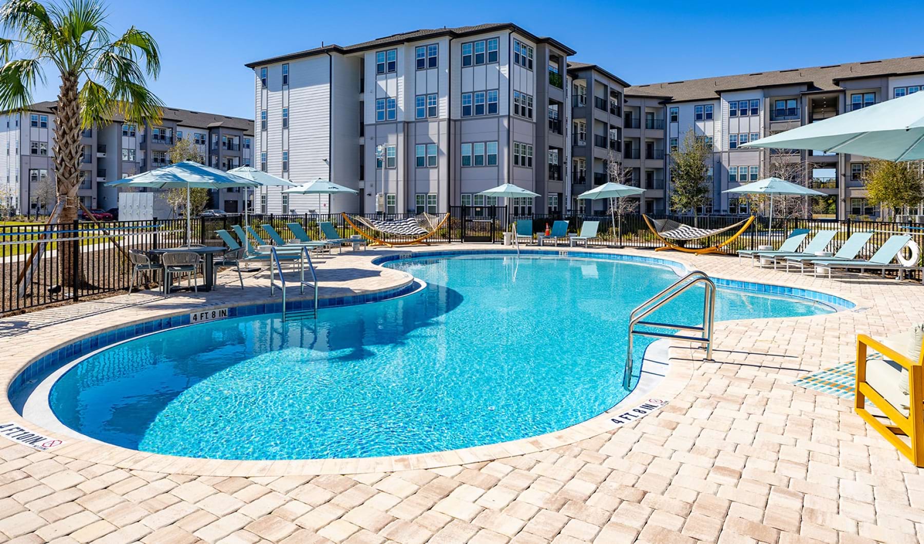 Sparkling resort-style swimming pool surrounded by lounge chairs at Solaris apartments, Kissimmee, FL.