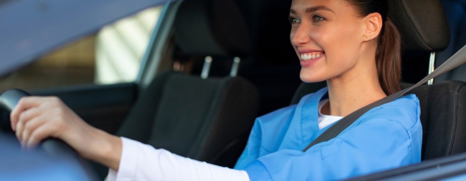 A smiling medical resident in blue scrubs driving a car in Kissimmee, Florida, representing housing for healthcare professionals.