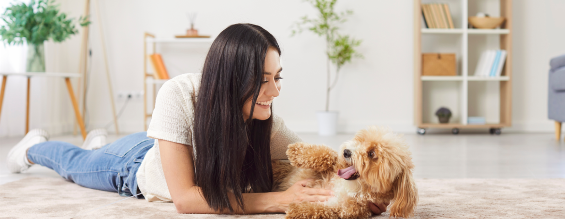 A smiling woman lying on a living room rug and playing with her happy, fluffy dog inside an apartment at Solaris in Kissimmee, Florida.