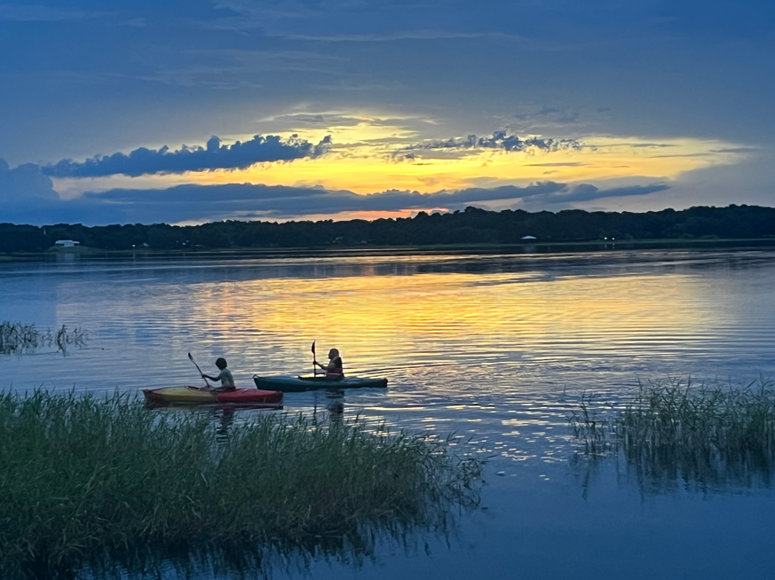 Two kayakers paddling on calm lake at sunset past marsh grass in St. Cloud Florida